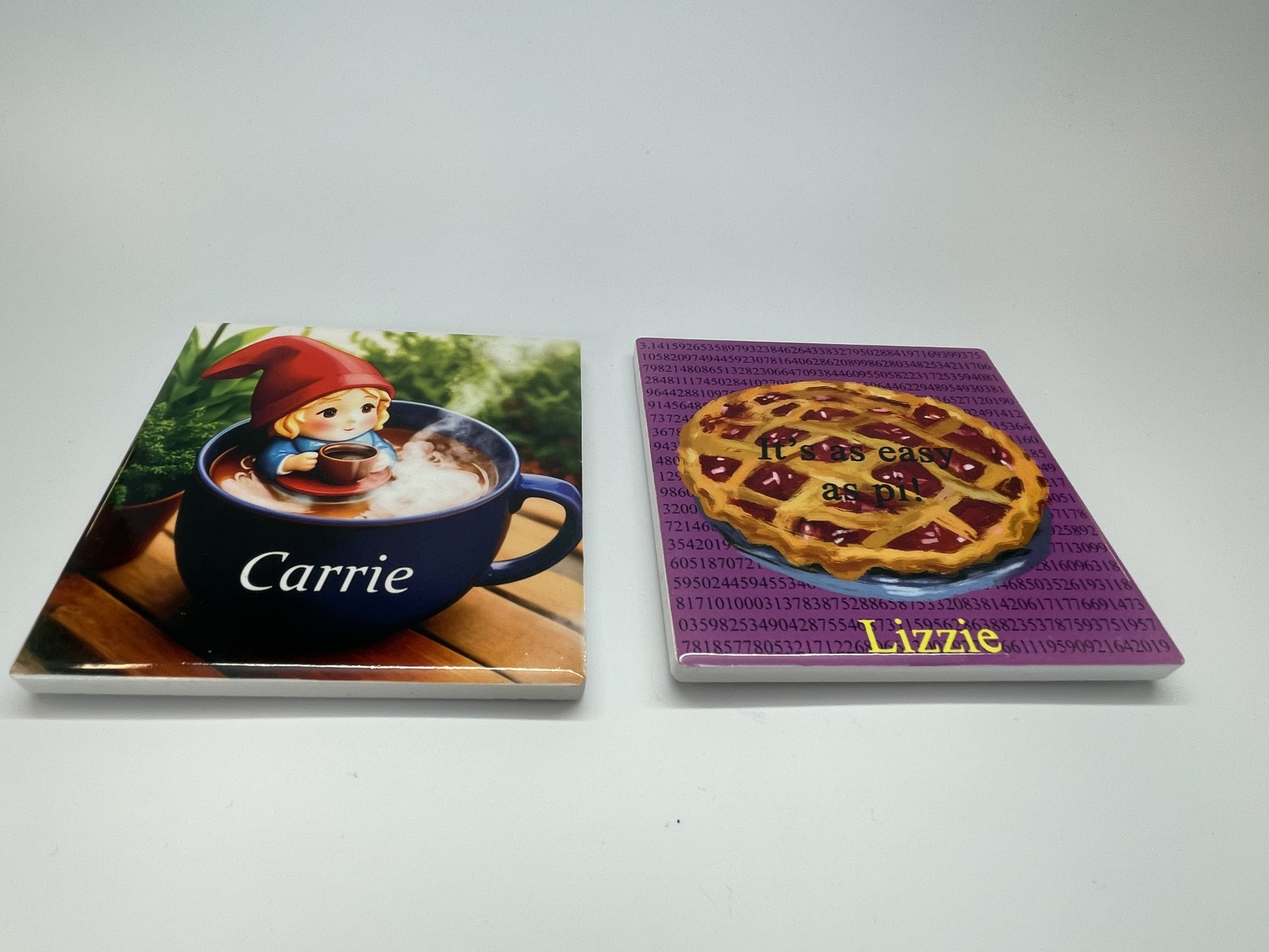 Two trivets: One labeled Carrie, picturing an elf sitting in a teacup drinking a cup of tea. The other labeled Lizzie, picturing a cherry pie with the words: It's as easy as pi!